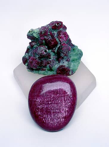 A fine Longido (Tanzania) ruby cabochon flanked by Longido ruby crystals in a green zoisite matrix.